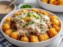 Crispy tater tots topped with sausage gravy, eggs, and melted cheese in a bowl.