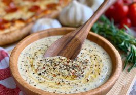 Creamy garlic sauce served in a bowl alongside pizza slices.