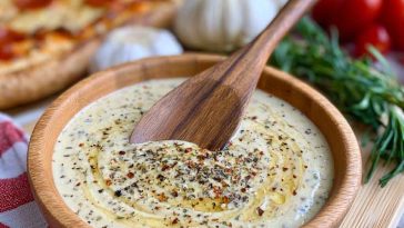 Creamy garlic sauce served in a bowl alongside pizza slices.