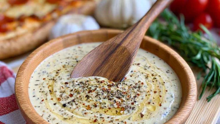 Creamy garlic sauce served in a bowl alongside pizza slices.