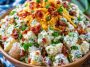Creamy loaded potato salad with tender potatoes, crispy bacon, shredded cheese, green onions, and a rich dressing.