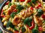 Chicken pasta with colorful vegetables including broccoli, bell peppers, and carrots in a light savory sauce.