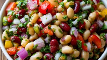 Colorful bean salad with mixed beans, fresh vegetables, herbs, and a tangy vinaigrette in a serving bowl.