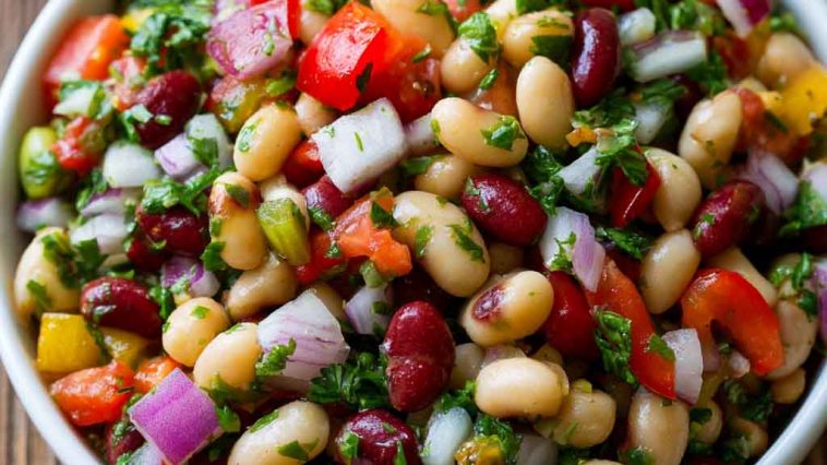 Colorful bean salad with mixed beans, fresh vegetables, herbs, and a tangy vinaigrette in a serving bowl.