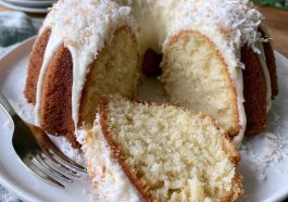 Moist coconut cream cheese pound cake topped with shredded coconut and sliced to reveal a rich buttery texture.