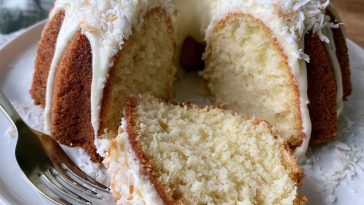 Moist coconut cream cheese pound cake topped with shredded coconut and sliced to reveal a rich buttery texture.