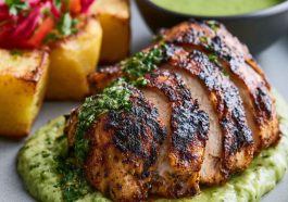 Roasted Peruvian chicken served with vibrant green sauce, crispy skin, and herbs on a plate.