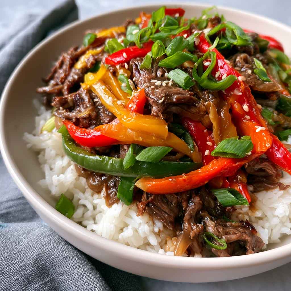 Healthy beef and pepper rice bowl with tender beef strips, colorful bell peppers, and fluffy rice, topped with fresh herbs.