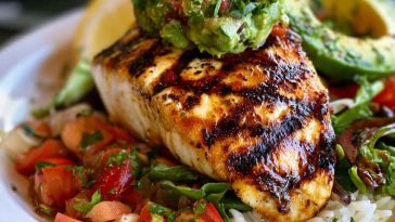 Grilled chicken breasts topped with fresh avocado slices, melted cheese, tomatoes, and herbs on a serving platter.