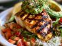 Grilled chicken breasts topped with fresh avocado slices, melted cheese, tomatoes, and herbs on a serving platter.