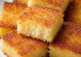 Golden coconut cake squares with a crispy caramelized top and soft, moist center served on a white plate for an easy homemade dessert.