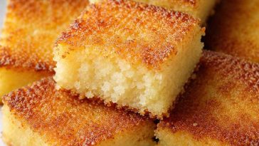 Golden coconut cake squares with a crispy caramelized top and soft, moist center served on a white plate for an easy homemade dessert.