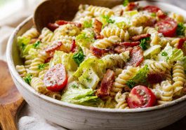 A large bowl of creamy BLT pasta salad with rotini pasta, crispy bacon pieces, halved cherry tomatoes, and fresh romaine lettuce.
