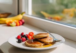 A stack of golden brown fluffy cottage cheese pancakes topped with fresh berries and a drizzle of maple syrup.